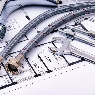 Braided supply lines, a faucet and a pipe wrench laid out on a bathroom floor plan